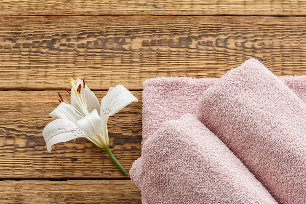 Soft terry towels with white lily flower on old wooden boards. Top view.