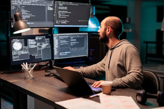 Software developer coding database on multiple monitors to program new server interface at night. Workign after hours to develop html source code on terminal window, artificial intelligence.