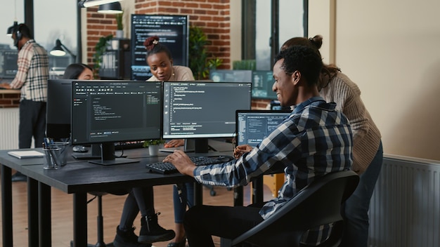 Software developer looking at running code on multiple screens takes off glasses and doing high five hand gesture with colleague programer. Programmers celebrating successful online cloud computing.