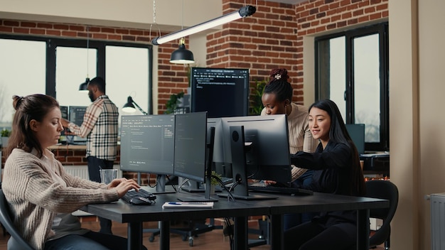 Software engineer typing source code on computer keyboard while colleagues sit down at desk for group project. App developer working in it startup company doing online cloud computing.