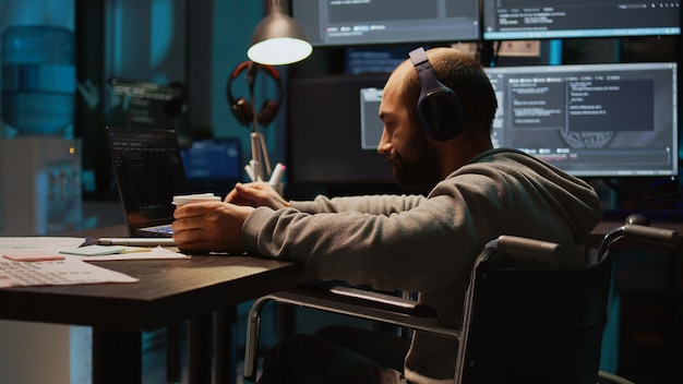 Software engineer using terminal window on laptop to program new code, dealing with physical impairment. Male web developer in wheelchair coding firewall security or html script. Handheld shot.