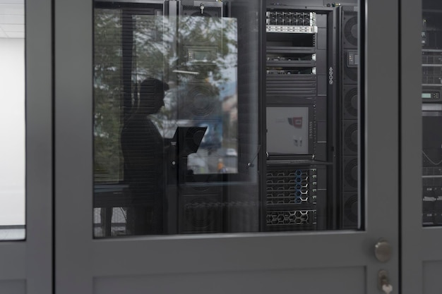 Software engineer working on a laptop computer in a modern\
server room. monitoring room big data scientist in reflection of\
the entrance door. high quality photo