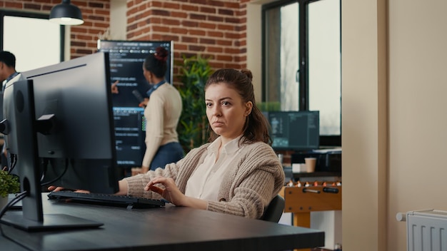 Software engineers analyzing code on wall screen tv looking for bugs and errors while colleague programer typing sitting at desk. App developers working on online cloud computing group project.