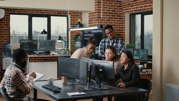 Software engineers brainstorming ideas looking at code on
computer screens asking feedback from senior developer while intern
joins the discussion. junior programmers collaborating on group
project.