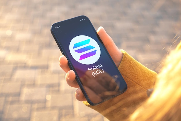 SolanaSOL暗号通貨シンボル。ビジネスと財務の概念。スマートフォンで手、暗号ロゴのクローズアップで画面
