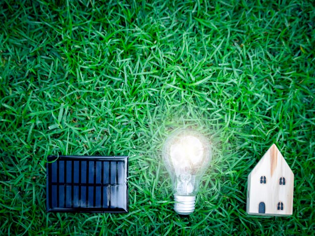 Solar cell light bulb and wooden house on green grass energysaving using renewable green energy for saving the world love and protect our planet environmental friendly concept