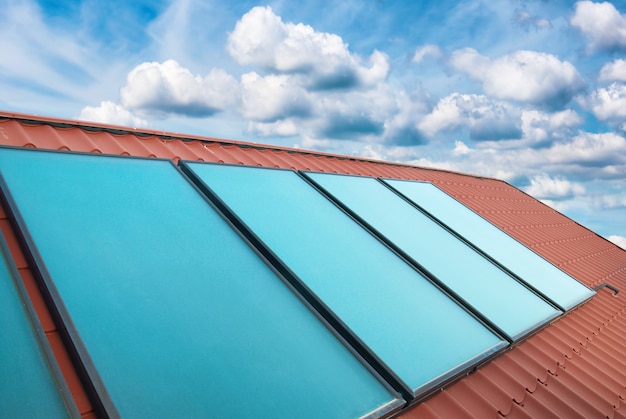 Солнечные батареи на крыше красного дома над голубым небом с облаками