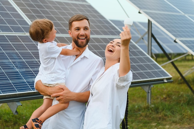 Концепция солнечной энергии Молодая счастливая семья стоит возле солнечных батарей и держит электрическую лампочку