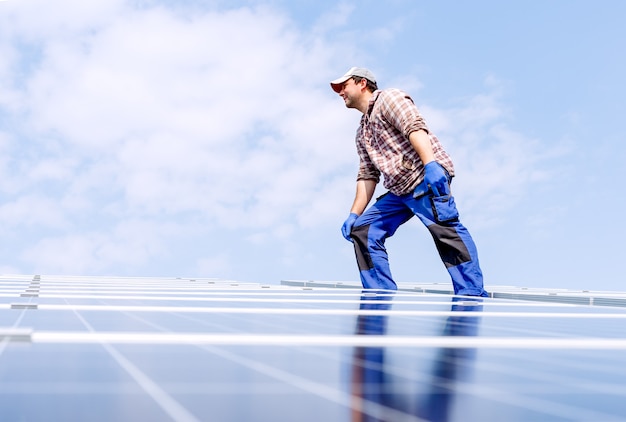 Energia del pannello solare. l'uomo dell'ingegnere elettrico sta lavorando nella stazione solare sul tetto contro il cielo blu in una giornata di sole. tecnologia di energia alternativa di sviluppo del sole. concetto ecologico.