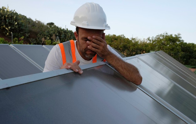 solar panel worker covers his face in desolation. Sad and sorrowful worker