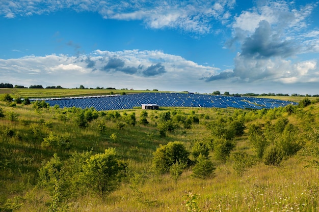 Solar panels station hills and bushes under blue sky on summer landscape