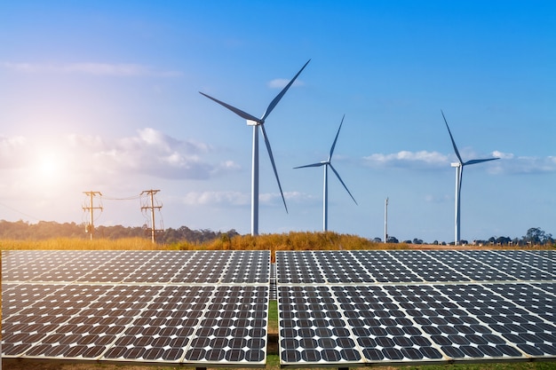 Solar panels with wind turbines against mountanis landscape against blue sky with clouds