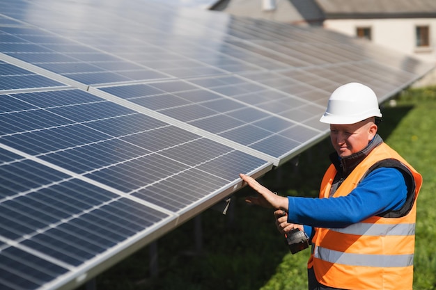 Solar power plant worker with electric wrench in his hands\
inspects panels