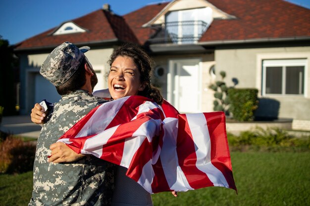 Soldaat die thuiskomt en zijn vrouw met Amerikaanse vlag die in zijn armen rent om de reünie te vieren