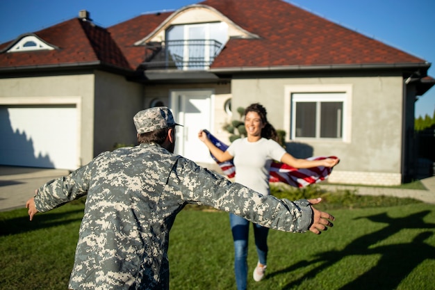 Soldaat die thuiskomt en zijn vrouw met amerikaanse vlag die in zijn armen rent om de reünie te vieren