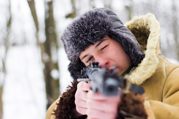 soldaat in bruine oude jas en bontmuts richt zich in de winter met een wapen in het bos