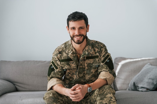 Soldaat in uniform is binnen in de huiskamer Zittend op de bank