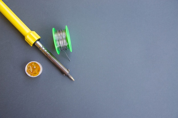 Soldering iron, tin, rosin on a black table. Soldering iron in male hands. Repair of electrical equipment, radio engineering. Solder wires, contacts.