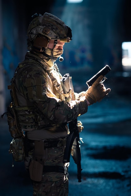 Солдат армейских элитных сил, боец специальной службы безопасности со скрытым лицом за маской и очками, в шлеме и системе грузовой тележки, целится из служебного пистолета с низким ключом. Фото высокого качества