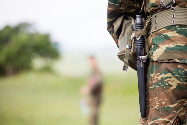 Soldier' body with camo clothing and knife in his belt Close up behind view blurred soldier and nature background copyspace