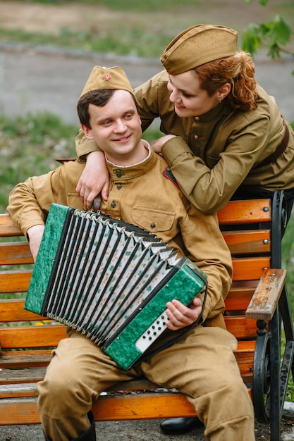 Фото Солдат сидит на скамейке, играет на баяне, а женщина-солдат