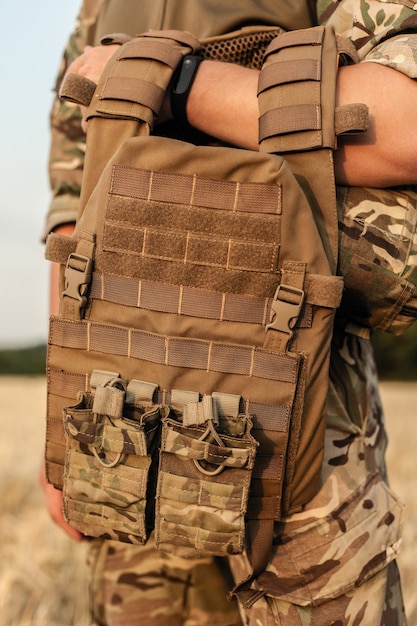 Soldier man standing against a field. soldier in military\
outfit with bulletproof vest. photo of a soldier in military outfit\
holding a gun and bulletproof vest on orange desert\
background.