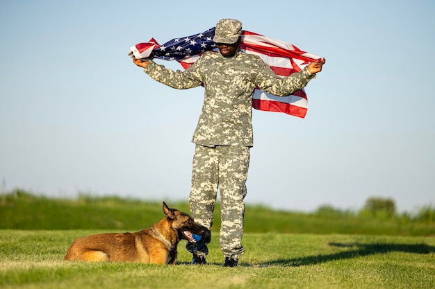 アメリカの国旗を持ち、犬と一緒に自由と愛国心を祝う軍服を着た兵士