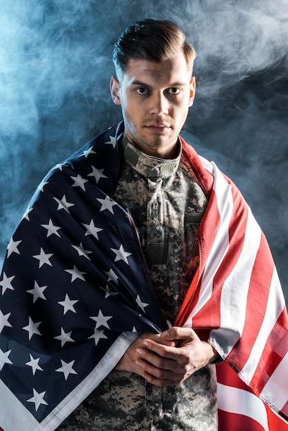 Soldier in military uniform with clenched hands and american flag looking at camera on black with