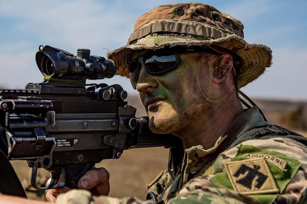 A soldier wearing a camouflage hat and sunglasses holds a gun with the number 7 on it.