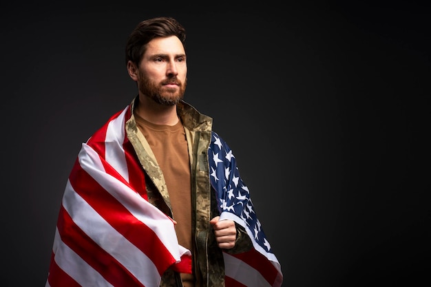 Soldier wearing military camouflage uniform holding American flag isolated on black background