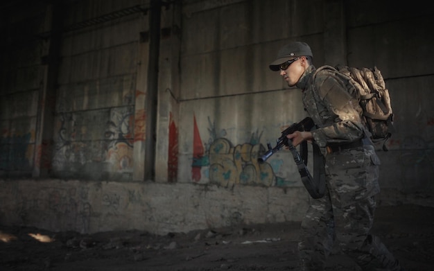 A soldier with a machine gun in his hands in a gray camouflage uniform in a cap and tactical glasses runs for cover