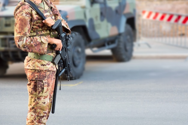 軍のSUV装甲車の近くのイタリアの制服を着たライフルを持った兵士。