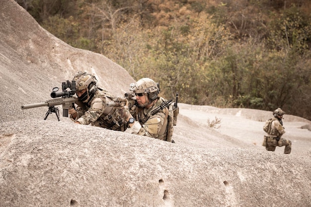 Soldiers in camouflage uniforms aiming with their rifles ready to fire during military operation