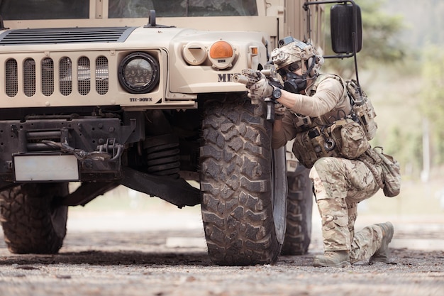 Foto soldati in uniforme di camuffamento tengono le armi pronte a sparare nascondendosi sul lato del veicolo militare