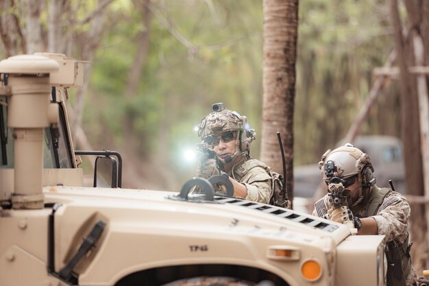 Photo soldiers in camouflage uniforms hold weapons ready to fire by hiding on the side military vehicle