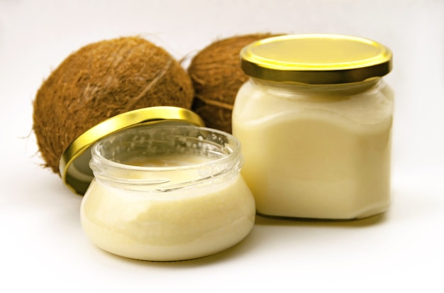 Solid homemade coconut oil in glass jar with metal gold lid and fresh coconuts on white  close up view. Selective soft focus. . Text copy space. Coconut butter concept