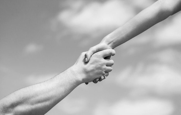 Solidarity compassion and charity rescue Hands of man and woman reaching to each other support Giving a helping hand Hands of man and woman on blue sky background Black and white