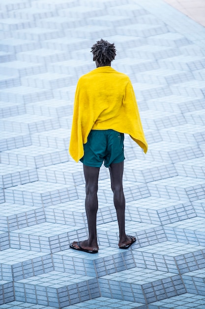 Solitario uomo nero africano, in pace con un asciugamano dopo aver lasciato la spiaggia in un ambiente urbano