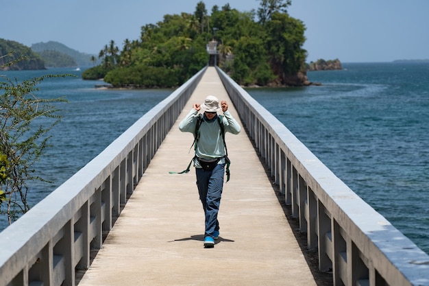 Solo hiker with backpack on bridge which leads to island travel and adventure concept