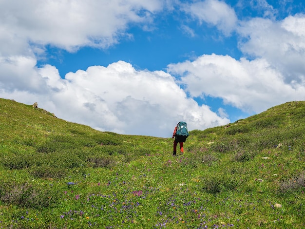 Solo hiking in the picturesque summer mountains. Heavy climb in the mountains with a backpack. Travel lifestyle, hiking hard track, adventure concept in summer vacation.