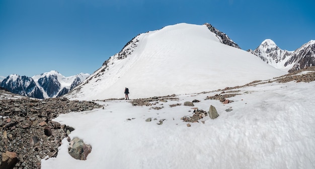 Solo-trekking in de bergen. Een mannelijke wandelaars langs het bergpad. Op de achtergrond grote besneeuwde bergen. Kopieer de ruimte, panoramisch uitzicht.