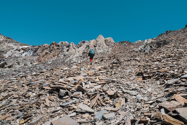 Trekking in solitaria in montagna l'uomo con un grande zaino si arrampica pesantemente su un sentiero di roccia sciolta avventura in solitaria concetto di stile di vita vacanze attive nel fine settimana nella natura selvaggia