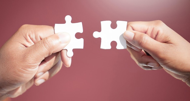 Solving the puzzle piece by piece Cropped shot of two unrecognizable businesspeople fitting puzzle pieces together in studio against a red background