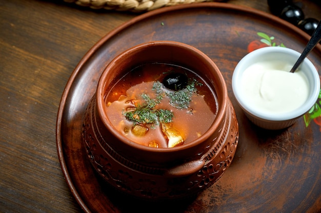 Solyanka meat soup with olives lemon smoked sausages in a bowl Wooden background