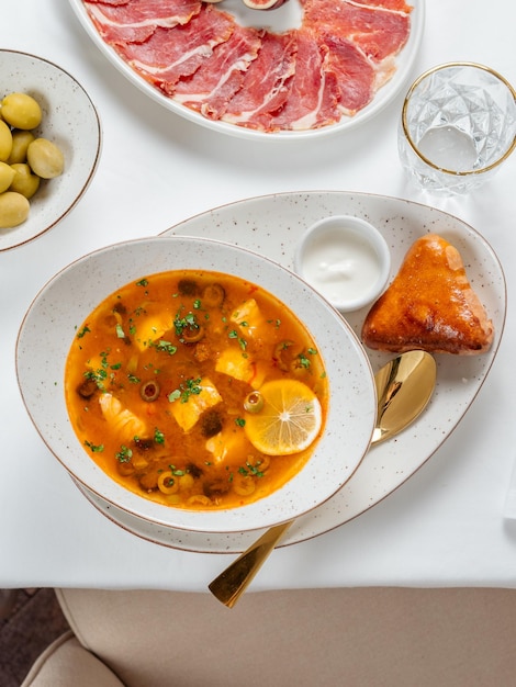 Photo solyanka soup with meat and olives garnished with a slice of lemon traditional russian meat soup solyanka in bowl on restaurant table top view or flat lay