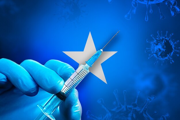Somalië Covid19 vaccinatiecampagne Hand in een blauwe rubberen handschoen houdt de spuit voor de vlag