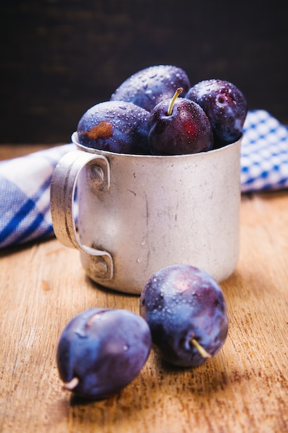 Some blue raw ripe plums in old cup in studio