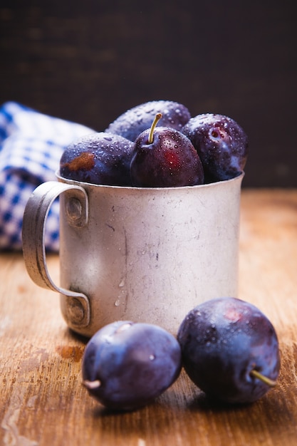 Some blue raw ripe plums in old cup in studio