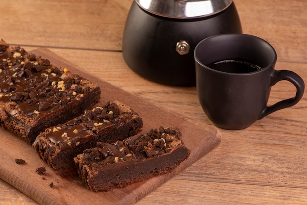 Alcune fette di brownie su legno, una caffettiera e una tazza di caffè.