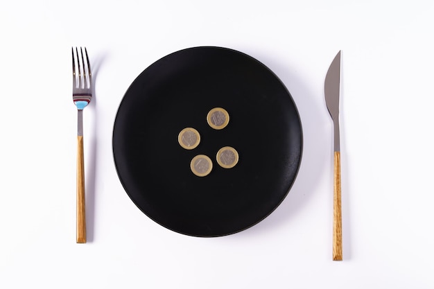 Some coins on a black plate isolated on a white background with a knife and fork